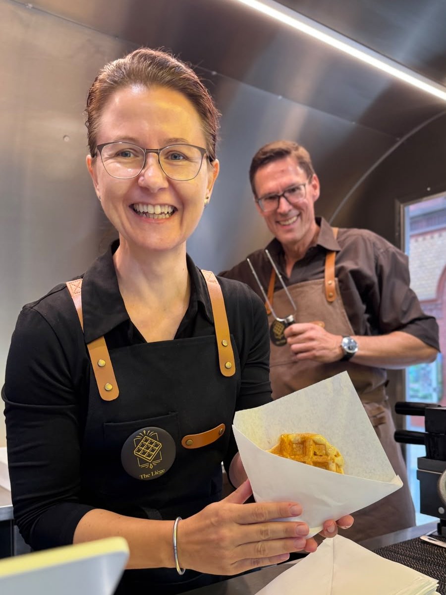 Nadine Rau reicht eine warme Lütticher Waffel, dahinter Mike Trepte mit der Waffelzange