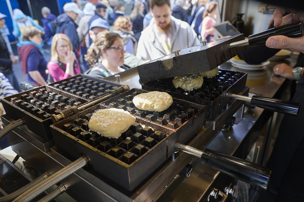 Waffelteig wird auf mehreren Eisen gebacken, im Hintergrund Gäste